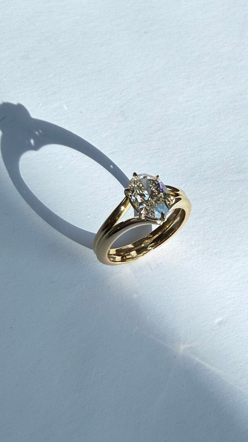 A gold ring with a clear round-cut gemstone, photographed on a white surface with a strong shadow.