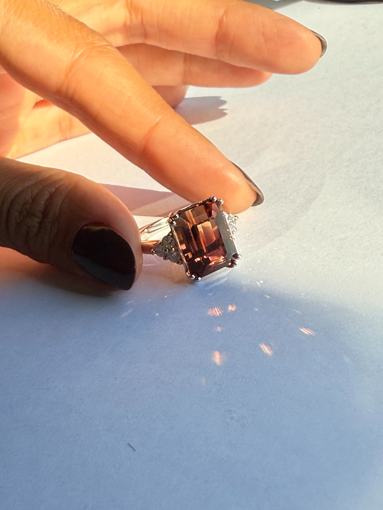 Person holding a ring with a large square gemstone on a light background