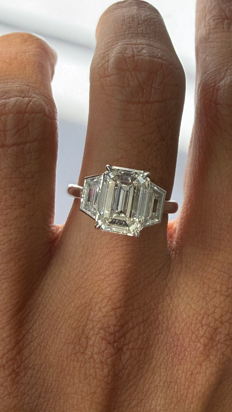 HAND WITH 4CT EMERALD DIAMOND RING WITH TRAPEZOIDS