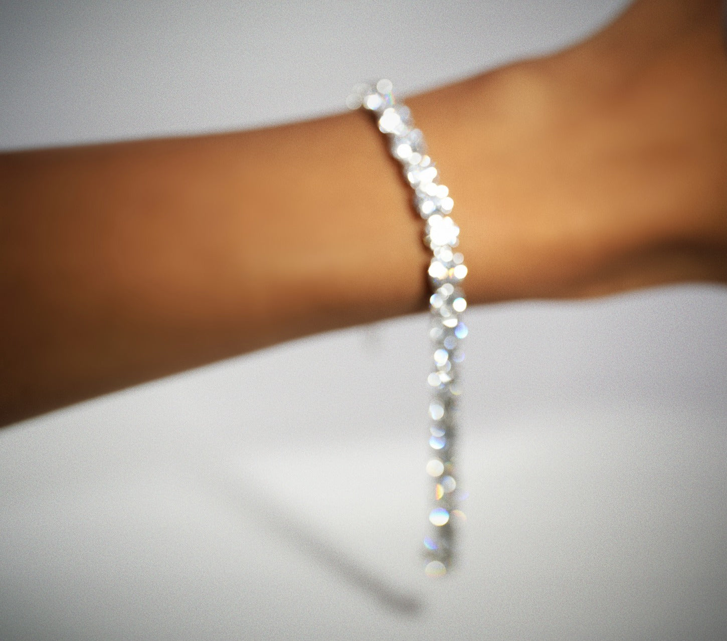 Close-up of a wrist wearing white gold diamond tennis bracelets on a neutral background
