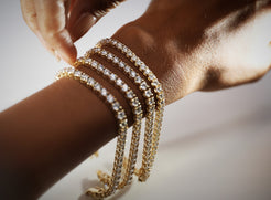 Close-up of a wrist wearing multiple carats weights of gold diamond tennis bracelets on a neutral background