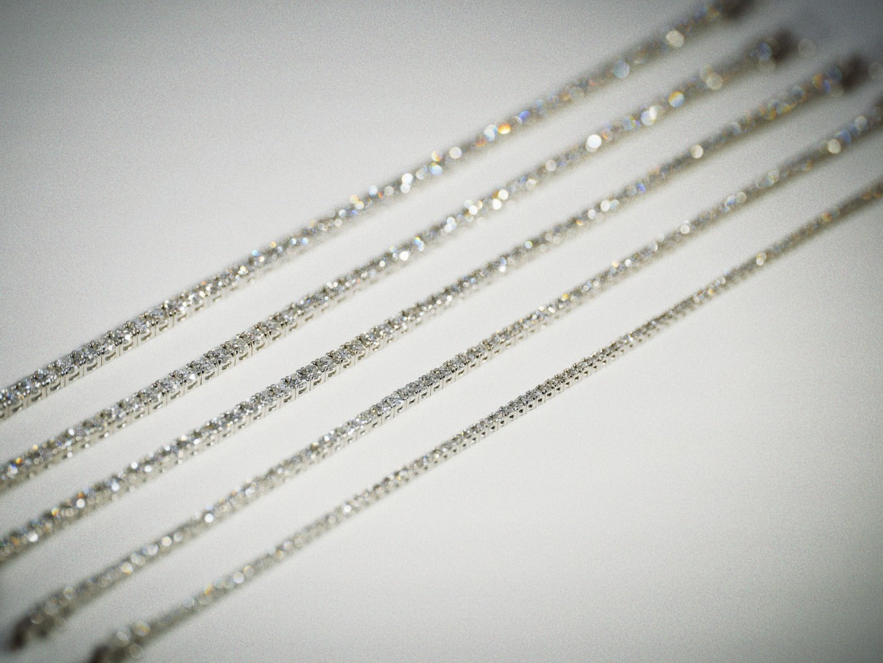Close-up of multiple carats weights of white gold diamond tennis bracelets on a neutral background