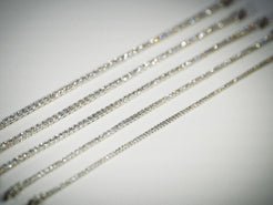 Close-up of multiple carats weights of white gold diamond tennis bracelets on a neutral background