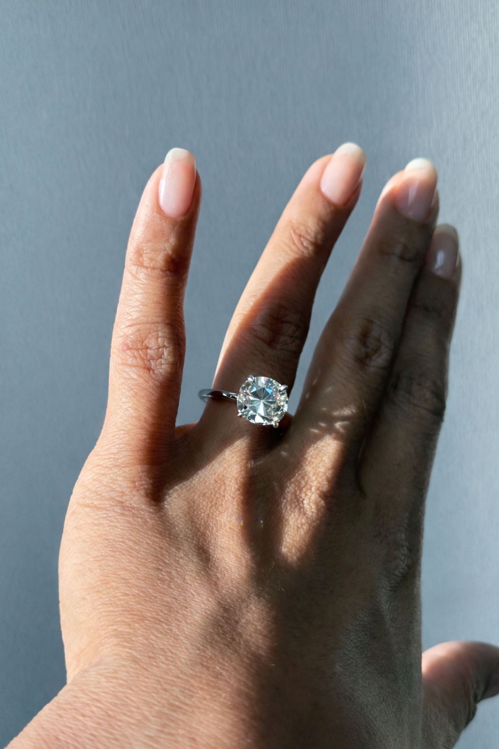 Hand wearing a diamond engagement ring against a neutral background